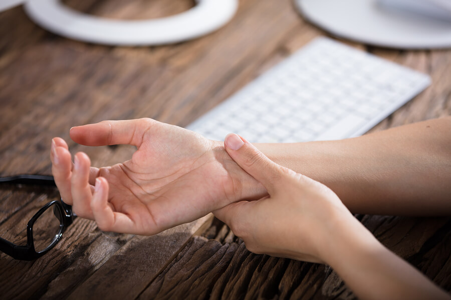 Close-up Of A Businessperson Holding Painful Wrist Over Wooden Desk