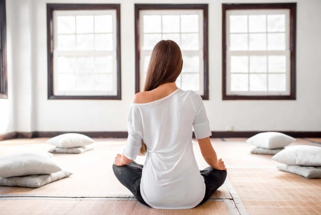 Young and positive woman in white t-shirt and black leggings practicing yoga in the bright interior with big windows.